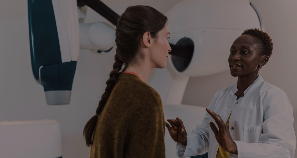 A clinician in a white coat talking with a patient beside imaging equipment